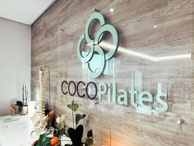 Dimensional Coco Pilates lettering and mint-green emblem on a wood-effect wall