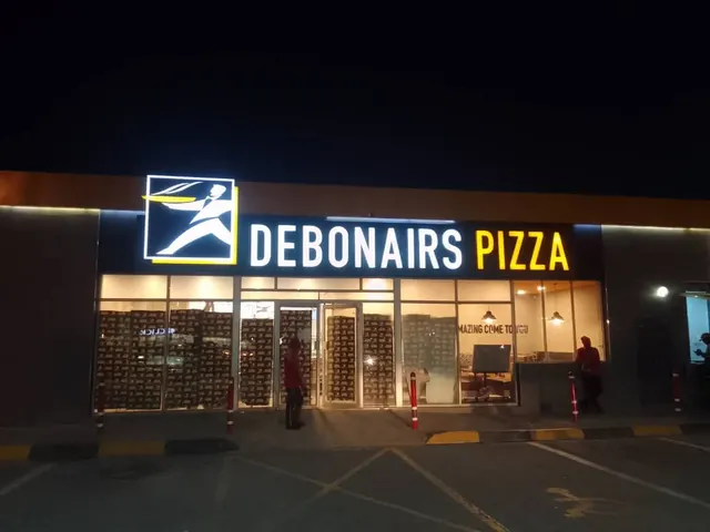 Illuminated Debonairs Pizza shopfront at Pilane Mall after dark